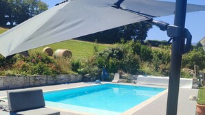 Un área junto a la piscina con piscina, sillas de descanso y una pérgola con sombrilla.