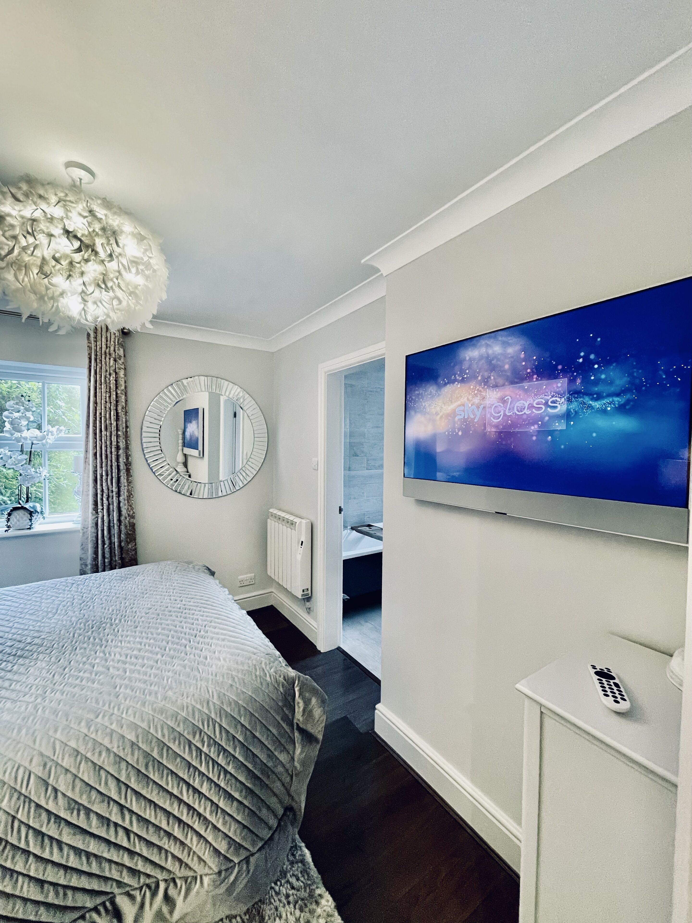 Moderni hotellihuone, jossa on suuri sänky, televisio, peili ja näkymä kylpyhuoneeseen.
