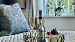 En seng med et dekorativt bakken med champagne, to glas og en skål med frugt.