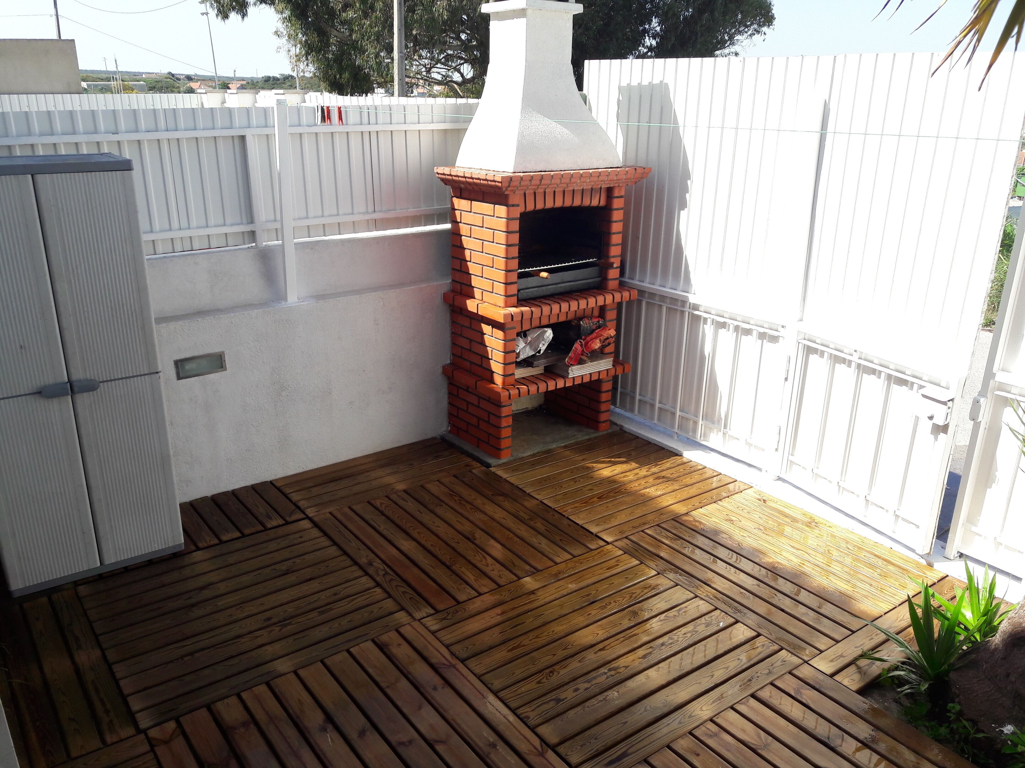Een barbecue buiten, gebouwd van bakstenen, met een schoorsteen, omringd door een witte hek en gelegen op een houten terras.