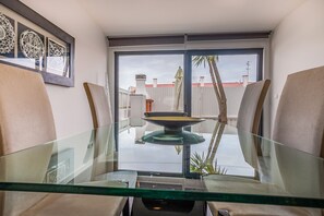 A dining area with a glass table and chairs, a decorative plate on the table, and a view of the outside through a large window.