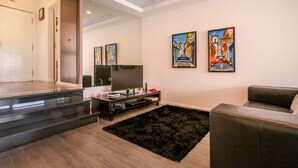 A modern living room with a flat-screen TV, a black leather sofa, and two colorful paintings on the wall.