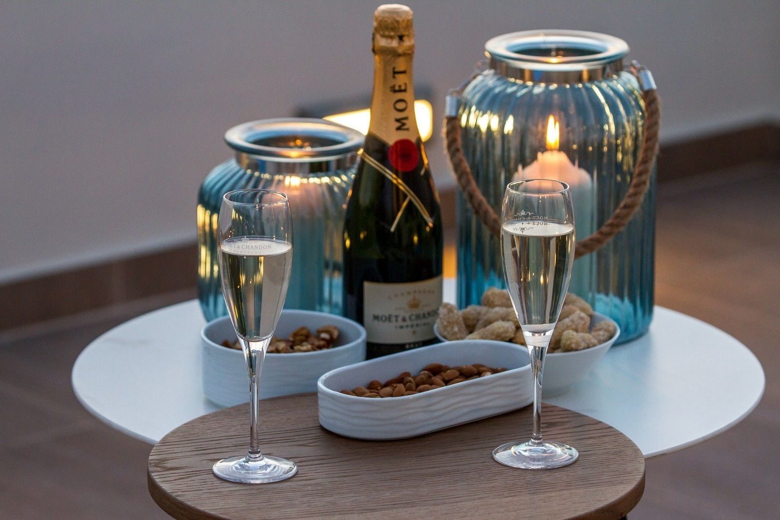 Zwei Sektgläser auf einem runden Holztisch, im Hintergrund eine Flasche Moët & Chandon und zwei Glasbehälter.