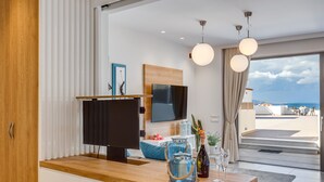 A modern kitchen with a wooden countertop, a flat-screen TV, and a view of the sea through large windows. - Angels Suites (Platanias)