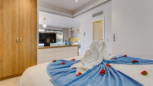 A modern hotel room with a large bed, a wooden wardrobe, a bathroom with a mirror, and a kitchen area. - Angels Suites (Platanias)