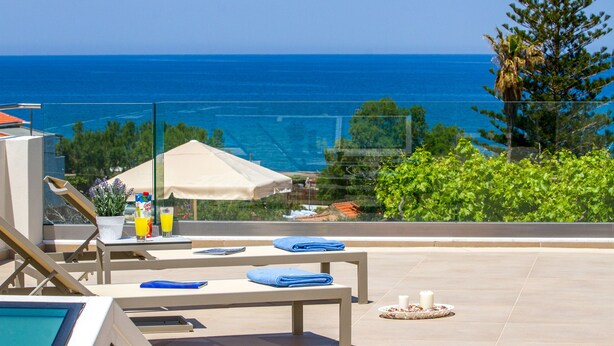 A poolside area with lounge chairs, a table with towels, and a view of the ocean. - Angels Suites (Platanias)