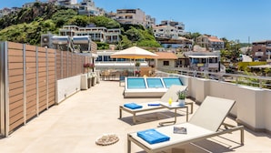 A rooftop terrace with lounge chairs, a pool, and a view of the cityscape. - Angels Suites (Platanias)