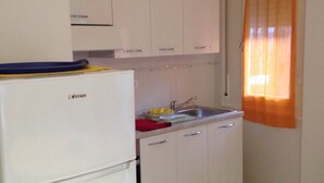 A compact kitchen with white cabinets, a refrigerator, a sink, and a window with orange curtains.