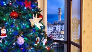 Un árbol de Navidad adornado con adornos y luces, un balcón con vistas a la ciudad y una puerta con papel tapiz estampado.