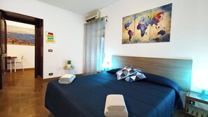 Ett hotellrum med en säng, ett konstverk i form av en världskarta, en växt och utsikt över ett kustnära område.
