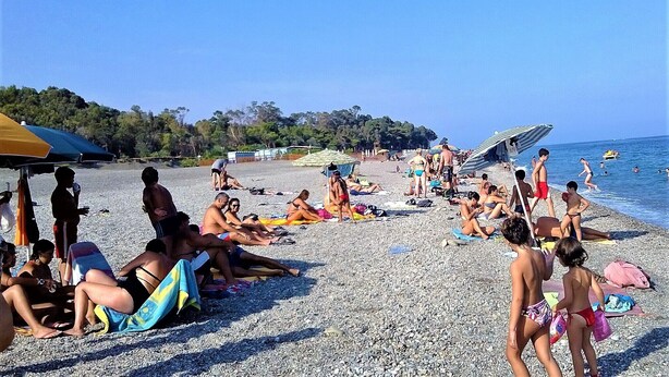 A crowded beach with people sunbathing and swimming.