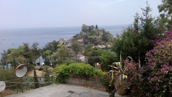 A coastal view with a historic building on a cliff, surrounded by greenery and a body of water.