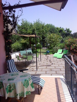 Un patio con mesa y sillas, una zona de estar cubierta y vistas al jardín.