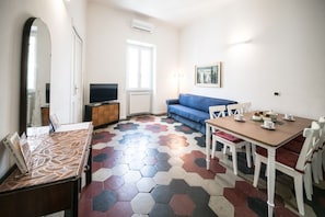 A room with a sofa, a dining table with chairs, a TV, and a patterned floor. - Relax Apartment Navona Sq. (Roma)