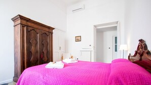 Une chambre à coucher avec un grand lit, une armoire en bois, un radiateur blanc et une porte donnant sur une autre pièce.