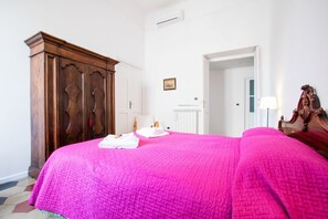 A bedroom with a large bed, a wooden wardrobe, a white radiator, and a door leading to another room.