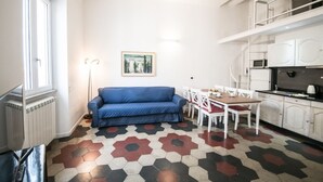 A compact living space with a blue sofa, a dining table with chairs, a kitchen area with cabinets, and a patterned floor. - Relax Apartment Navona Sq. (Roma)
