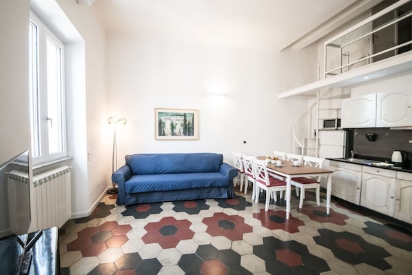 A compact living space with a blue sofa, a dining table with chairs, a kitchen area with cabinets, and a patterned floor. - Relax Apartment Navona Sq. (Roma)