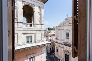 Blick auf eine enge Straße mit historischen Gebäuden, darunter ein Gebäude mit Balkon und Rundbogenfenstern.