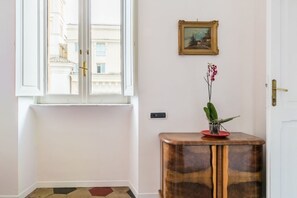 A room with a window, a door, a wall-mounted picture, and a small wooden table with a plant. - Relax Apartment Navona Sq. (Roma)