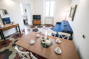 A dining area with a table set for tea, white chairs, a sofa, and a TV in the background. - Relax Apartment Navona Sq. (Roma)