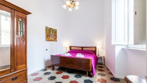A bedroom with a wooden wardrobe, a bed with a pink bedspread, a painting on the wall, and a geometric-patterned floor. - Relax Apartment Navona Sq. (Roma)