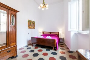 Una camera da letto con un armadio in legno, un letto con copripiumino rosa, un quadro appeso al muro e un pavimento con motivi geometrici.