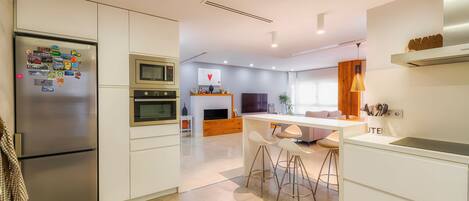 Una cocina moderna con refrigerador, horno, microondas y taburetes de bar.