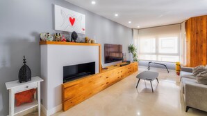 Uma sala de estar moderna com televisão de tela plana, móvel para home theater em madeira e um sofá cinza.