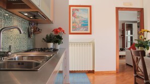 A kitchen with a stainless steel sink, a stove, and a potted plant with red flowers.