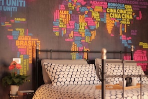 Un lit avec des coussins à motifs et, en arrière-plan, un mur décoré d’une carte du monde.