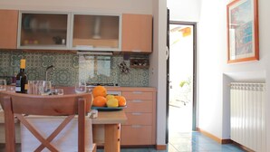 A kitchen with a dining table, a fruit bowl, and a bottle of wine.