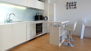 Een moderne keuken met witte kastjes, een inbouwoven, een koffiezetapparaat en een bar met twee krukken.