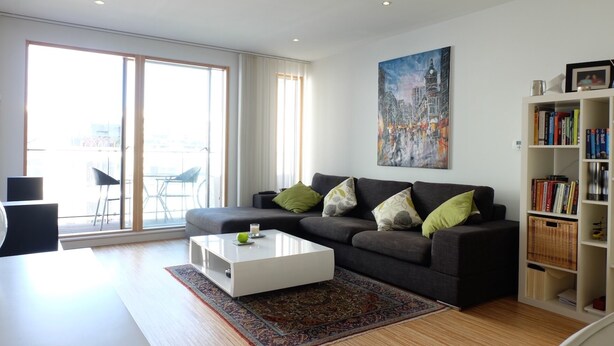 Een moderne woonkamer met een grijze bank, een witte salontafel en een boekenplank vol boeken.