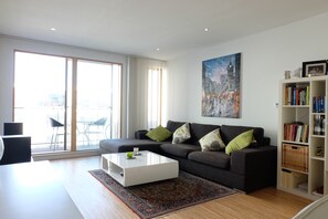 A modern living room with a grey sofa, a white coffee table, and a bookshelf filled with books. - Beautiful & Perfectly Located Ultra-Modern Flat (London)