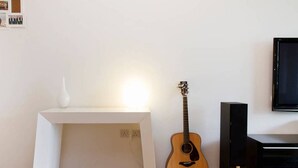 Een kamer met een witte console tafel, een gitaar, een witte vaas en een zwarte speaker.