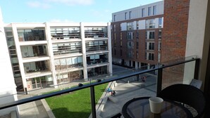 Een balkon met glazen hekwerk met uitzicht op een binnenplaats, met een gebouw op de achtergrond.