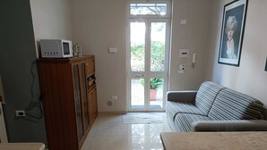 Un salón con sofá, un aparador de madera, microondas y una puerta que da al exterior.