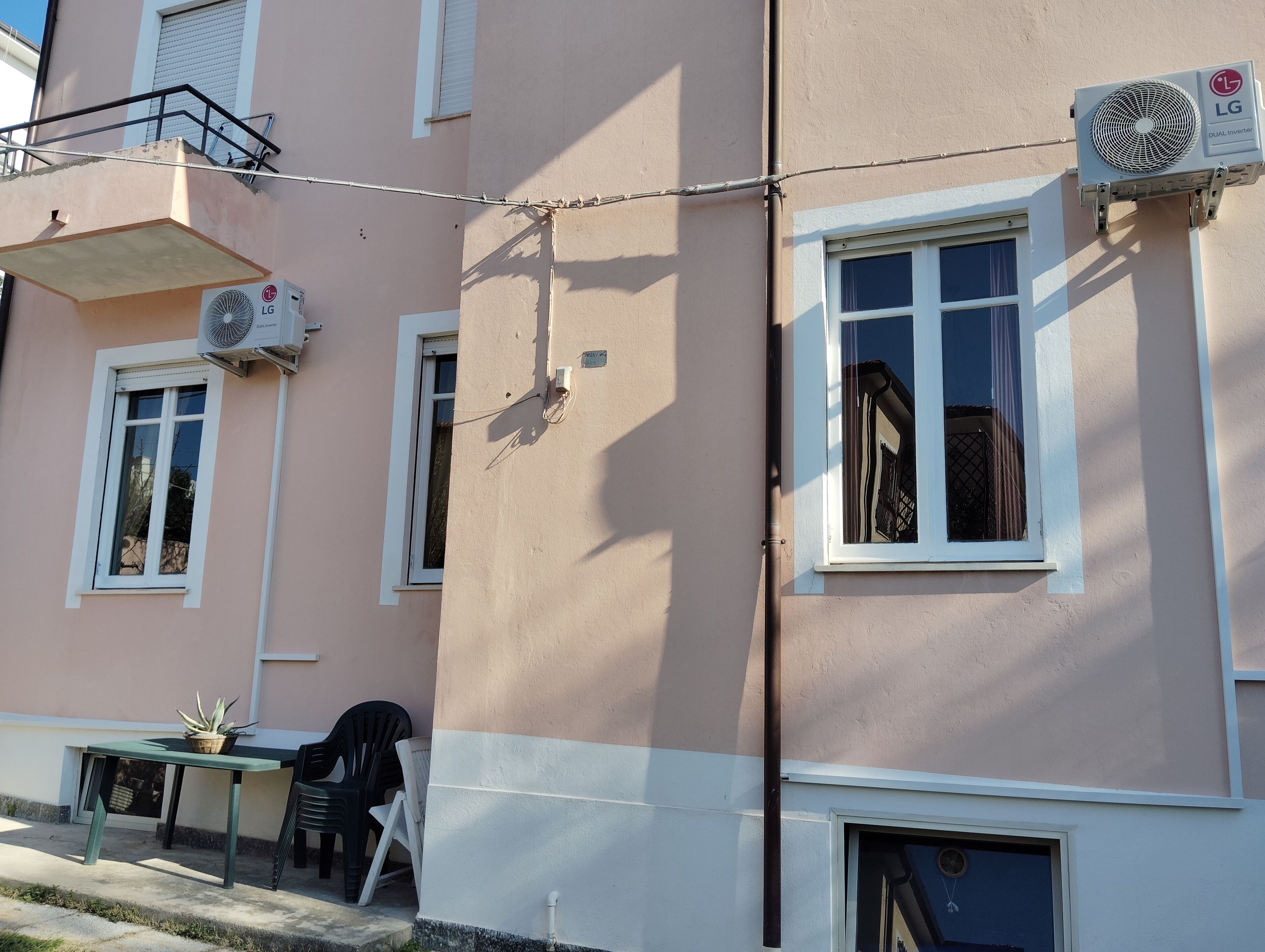 Un edificio con balcón, aire acondicionado y una mesa con sillas afuera.