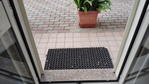 Puerta que da a un área empedrada con una planta en maceta y un felpudo.