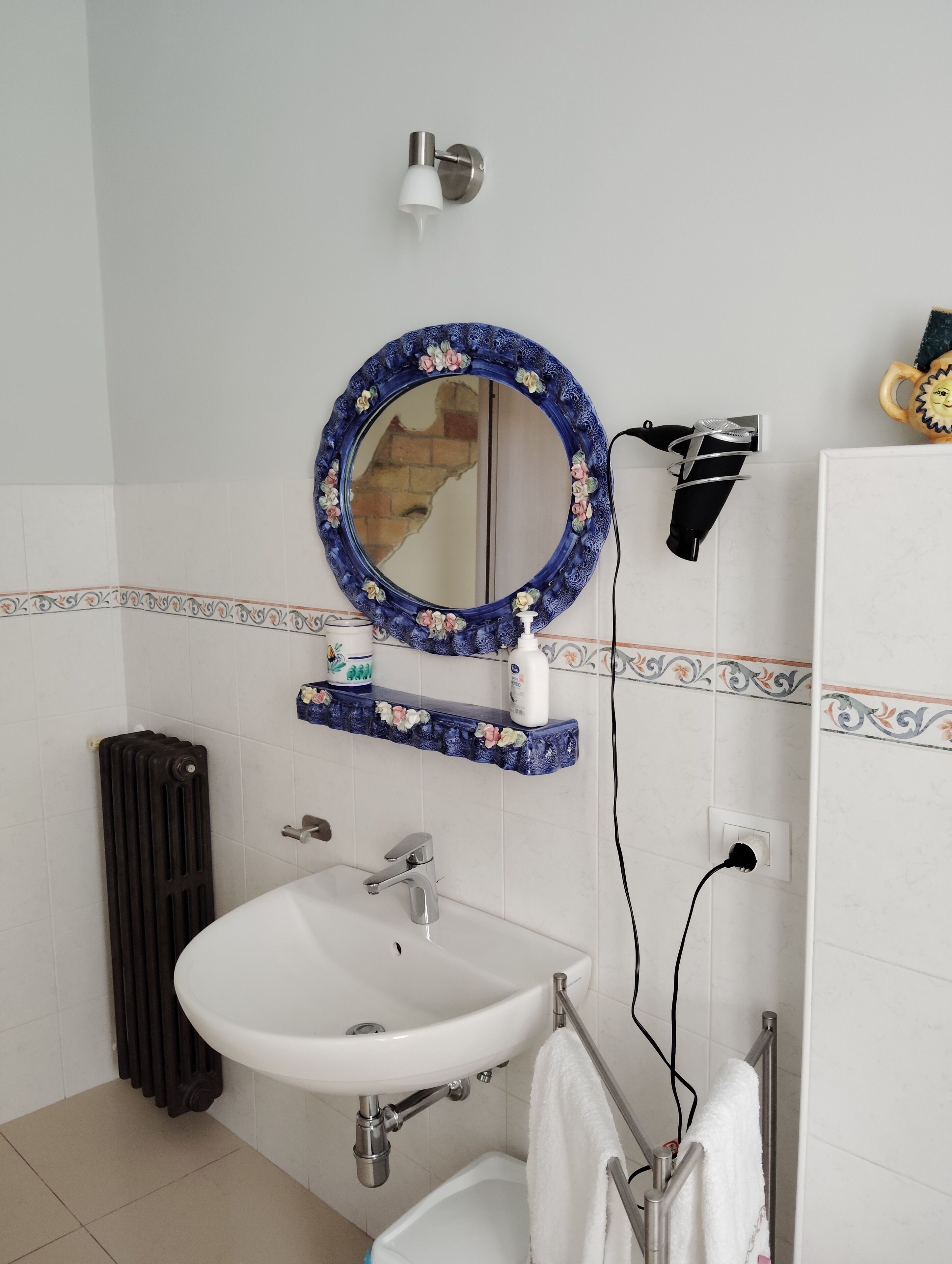 A bathroom with a white sink, a mirror with a floral frame, a towel rack, and a radiator.