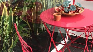 A red metal table with a bowl of dried flowers and a small pot on it, surrounded by green plants. - Traditional Angra House (Angra do Heroísmo)