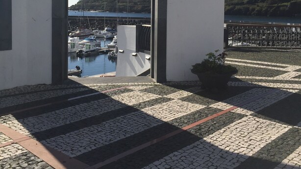 A view through an arched doorway to a marina with boats, a mountainous backdrop, and a paved area with a potted plant. - Traditional Angra House (Angra do Heroísmo)