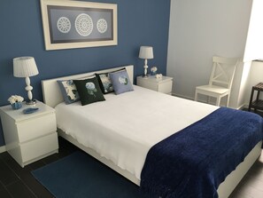 A neatly arranged bedroom with a bed, two bedside tables, a nightstand, a chair, and a framed artwork on the wall. - Traditional Angra House (Angra do Heroísmo)