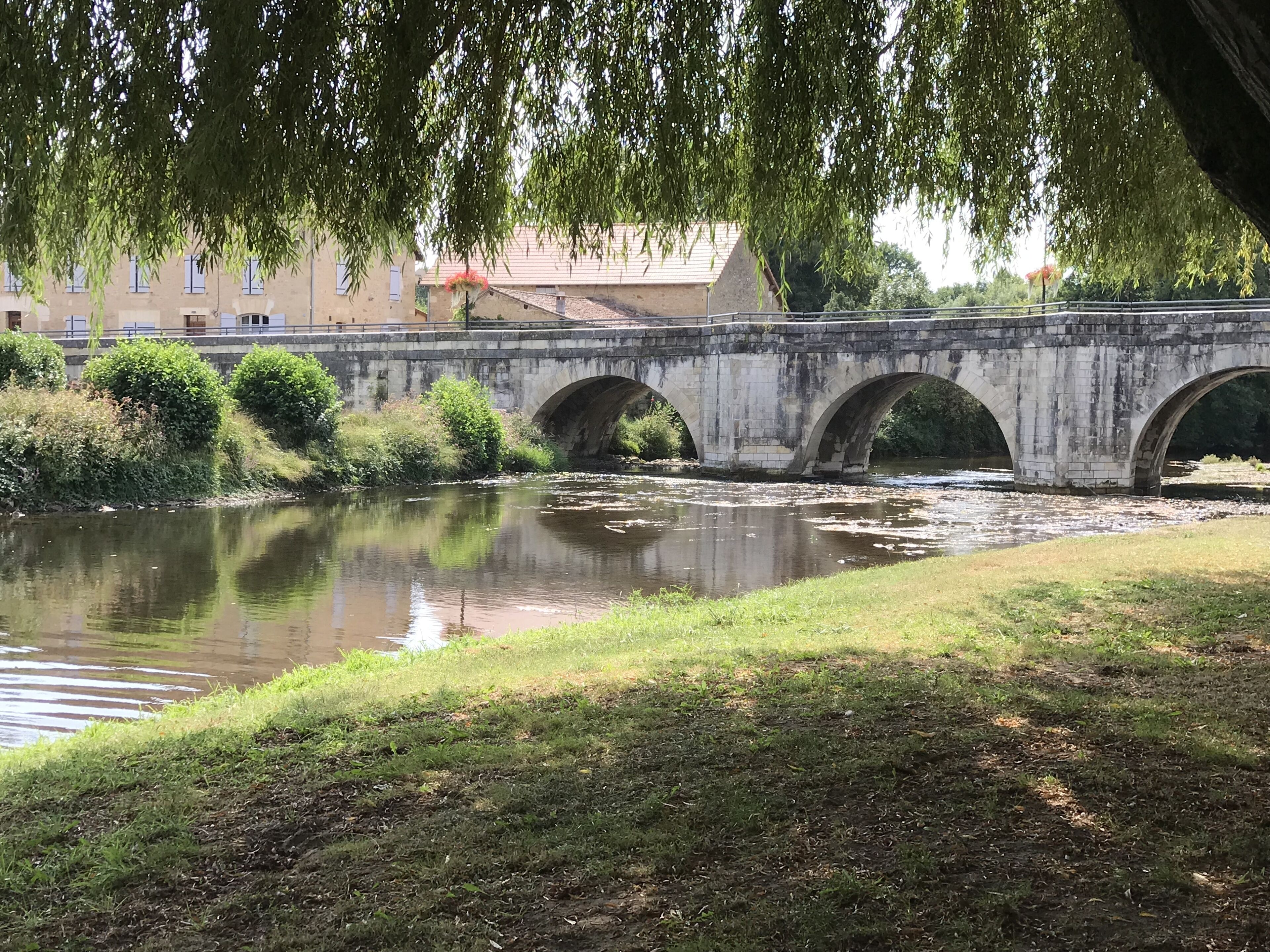 Un pont de pierre enjambe une rivière, et de chaque côté, la végétation est luxuriante.
