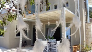 Een overdekt terras met witte meubels, hangende lantaarns en decoratieve veertjes.