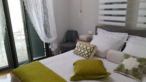 Een slaapkamer met een bed, kussens, een stoel, een nachtkastje en een raam met gordijnen.