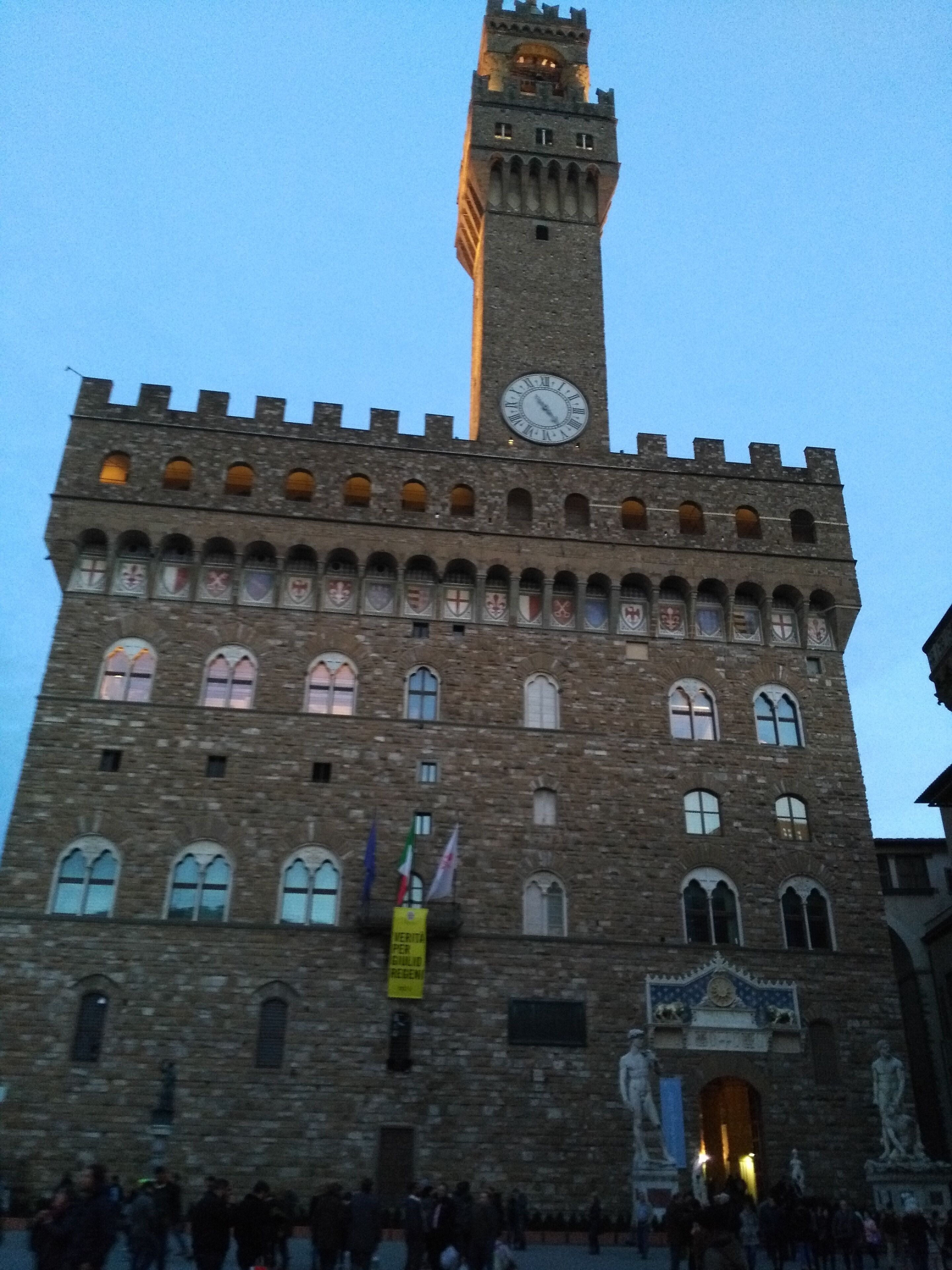 A historic building with a clock tower, arched windows, and flags.