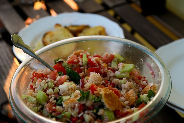 A bowl of salad with a spoon, and a plate with toast in the background.