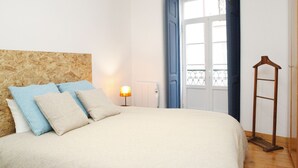 Une chambre à coucher avec un lit, des oreillers, une table de chevet, une lampe, un radiateur, une porte et une échelle en bois.